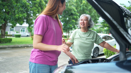 Grandmother and grandchild help each other execute a basic engine check on their parents' automobileの写真素材
