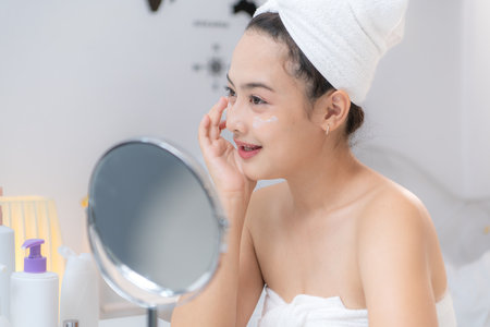 Asian young woman with towel wrapped on head and body applying makeup after shower, Morning beauty routine before workの写真素材
