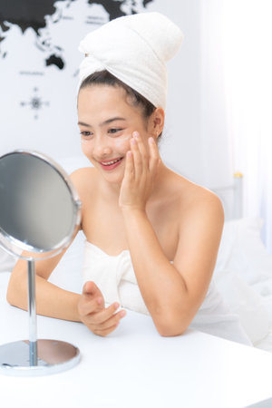 Asian young woman with towel wrapped on head and body applying makeup after shower, Morning beauty routine before workの写真素材
