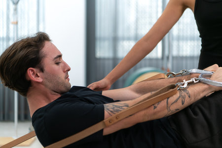 A young man and a young woman are doing pilates exercises on a pilates reformerの写真素材