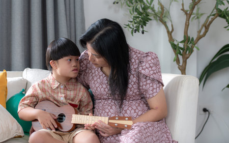A special child with his mom plays the ukulele in the living room of the house