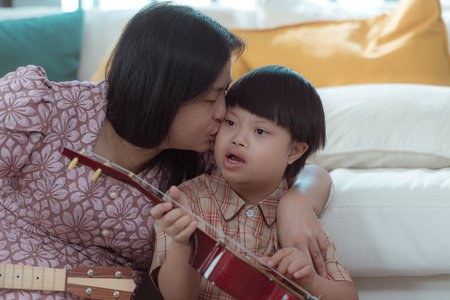 A special child with his mom plays the ukulele in the living room of the houseの写真素材