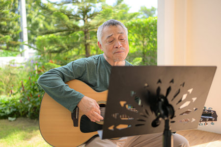 Senior man a veteran guitarist plays music in the garden at homeの写真素材