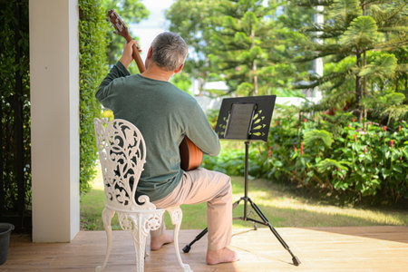 Senior man a veteran guitarist plays music in the garden at homeの写真素材