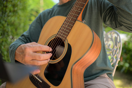 Senior man a veteran guitarist plays music in the garden at home