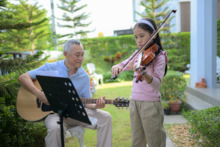 A girl violinist and her grandfather practice music together in the garden at homeの写真素材