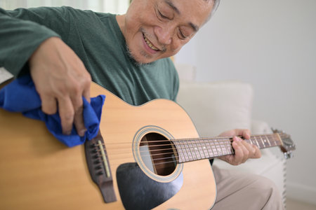 Senior man a veteran guitarist clean and repair the guitar at homeの写真素材