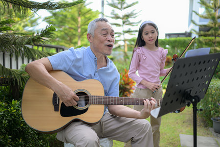 A girl violinist and her grandfather practice music together in the garden at homeの写真素材