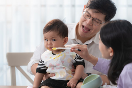 Father and mother feed their son breakfast before going to work in the kitchen of the houseの写真素材