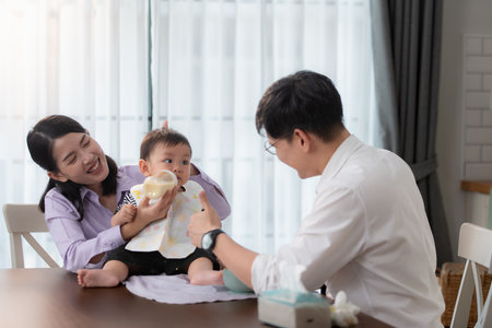 Father and mother feed their son breakfast before going to work in the kitchen of the houseの写真素材