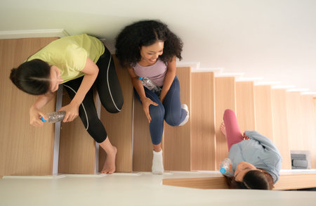 A group of young sports women breaks and drinks water in the staircase after yoga practice