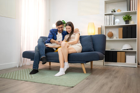 Young couple are smiling while relax and working online via laptop in living room at homeの写真素材