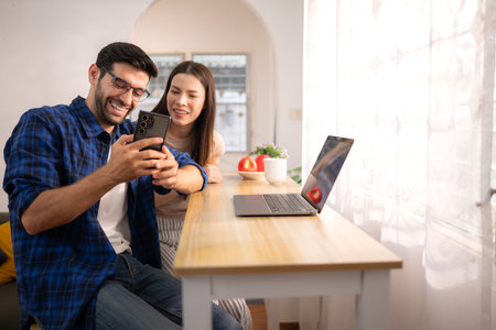 Portrait of a young freelancer smiling while working online via laptop at home with his girlfriendの写真素材