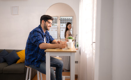 Portrait of a young freelancer smiling while working online via laptop at home with his girlfriendの写真素材