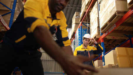 Two warehouse workers are lifting boxes of merchandise on a pallet jack to store on a shelf in a warehouseの写真素材