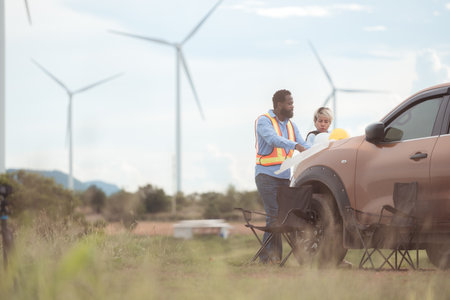An engineer father and his family do a little more work in front of a car before getting off work in a wind turbine fieldの写真素材