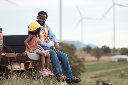 Sitting in the back of a car in a wind turbine field are a father engineer and his daughterの写真素材
