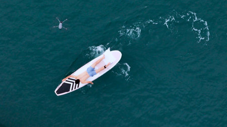 A young man is enjoying his ocean adventure aboard a yacht and surfboardの写真素材
