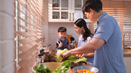 Happy Asian parents enjoying mealtime with their toddler in the kitchen, sharing laughter and playful moments during feeding timeの写真素材