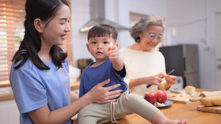 Happy Asian family preparing food together in a bright kitchen, sharing joyful moments with a toddler during a fun and healthy cooking timeの写真素材