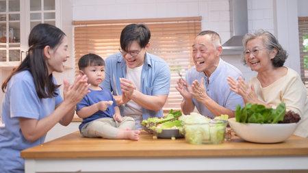 Happy Asian family preparing food together in a bright kitchen, sharing joyful moments with a...