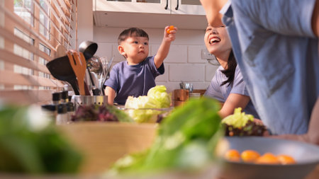 Happy Asian parents enjoying mealtime with their toddler in the kitchen, sharing laughter and playful moments during feeding timeの写真素材