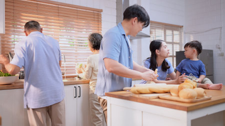 Happy Asian family preparing food together in a bright kitchen, sharing joyful moments with a toddler during a fun and healthy cooking timeの写真素材