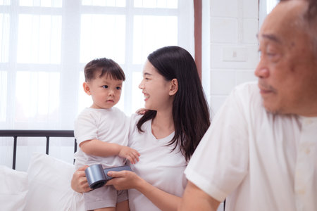 Before putting the kids to bed, mother, grandfather, and kid unwind and play in the bedroomの写真素材
