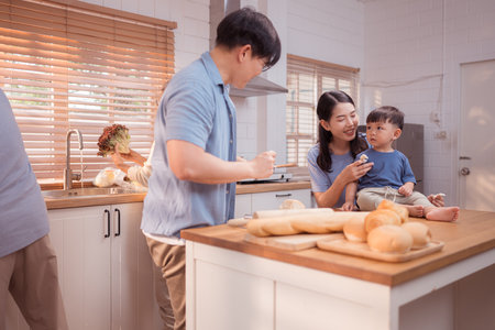 Happy Asian family preparing food together in a bright kitchen, sharing joyful moments with a toddler during a fun and healthy cooking timeの写真素材