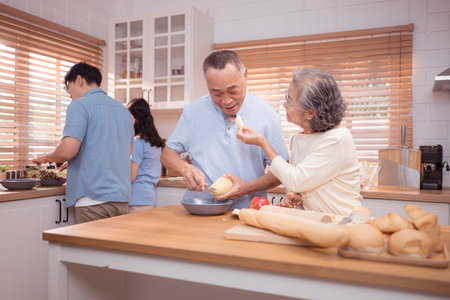 Happy Asian family preparing food together in a bright kitchen, sharing joyful moments with a toddler during a fun and healthy cooking timeの写真素材