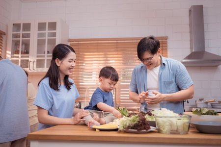 Happy Asian family preparing food together in a bright kitchen, sharing joyful moments with a toddler during a fun and healthy cooking timeの写真素材