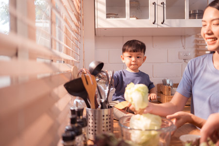 Happy Asian parents enjoying mealtime with their toddler in the kitchen, sharing laughter and playful moments during feeding timeの写真素材