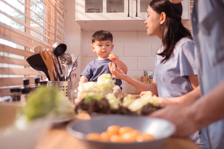 Happy Asian parents enjoying mealtime with their toddler in the kitchen, sharing laughter and playful moments during feeding timeの写真素材