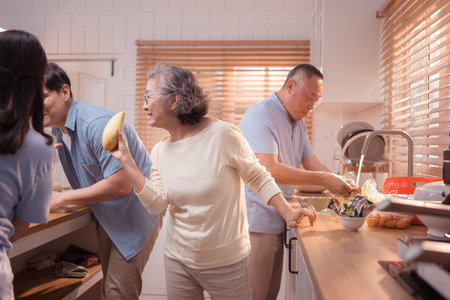 Happy Asian family preparing food together in a bright kitchen, sharing joyful moments with a toddler during a fun and healthy cooking timeの写真素材