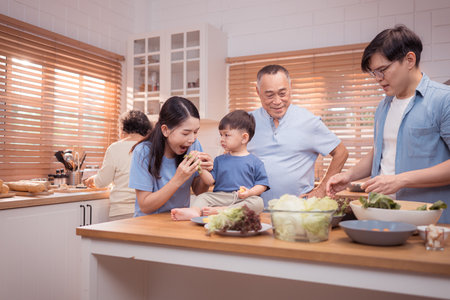Happy Asian family preparing food together in a bright kitchen, sharing joyful moments with a toddler during a fun and healthy cooking timeの写真素材