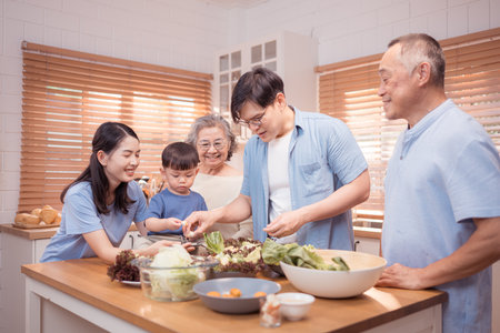 Happy Asian family preparing food together in a bright kitchen, sharing joyful moments with a toddler during a fun and healthy cooking timeの写真素材