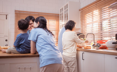 Happy Asian family preparing food together in a bright kitchen, sharing joyful moments with a toddler during a fun and healthy cooking timeの写真素材
