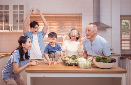 Happy Asian family preparing food together in a bright kitchen, sharing joyful moments with a...
