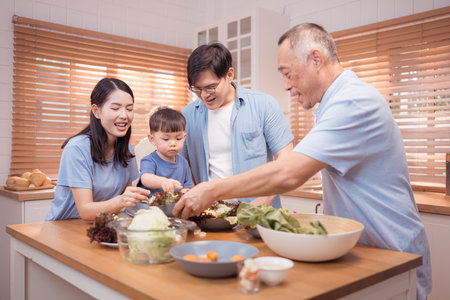 Happy Asian family preparing food together in a bright kitchen, sharing joyful moments with a toddler during a fun and healthy cooking timeの写真素材