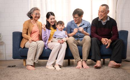 Happy multi-generational Asian family enjoying quality time together at home, cheering and smiling with a toddlerの写真素材