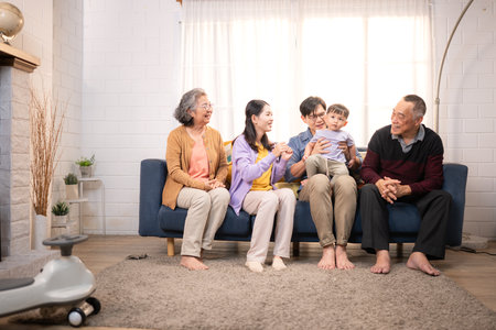 Happy multi-generational Asian family enjoying quality time together at home, cheering and smiling with a toddler riding a toy car in a cozy living roomの写真素材