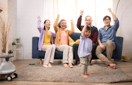 Happy multi-generational Asian family enjoying quality time together at home, cheering and smiling with a toddlerの写真素材