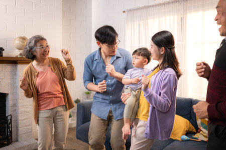 Happy multi-generational Asian family enjoying quality time together at home, cheering and smiling with a toddlerの写真素材