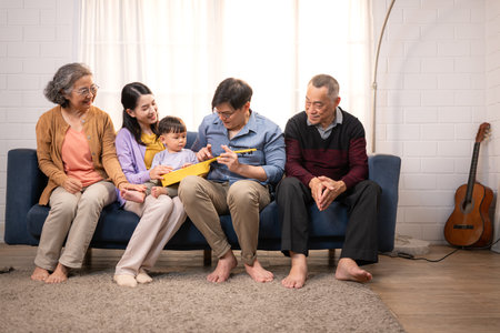 Happy multi-generational Asian family enjoying quality time together at home, cheering and smiling with a toddlerの写真素材