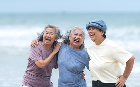 Happy senior women enjoying a playful walk on the beach, laughing and holding hands as they splash...