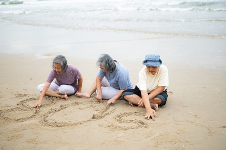 Happy senior women enjoying a playful walk on the beach, laughing and holding hands as they splash through the waves togetherの写真素材