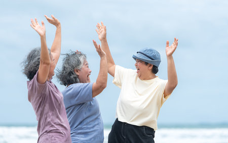 Happy senior women enjoying a playful walk on the beach, laughing and holding hands as they splash...