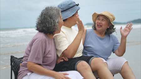 Happy senior women enjoying a playful walk on the beach, laughing and holding hands as they splash...