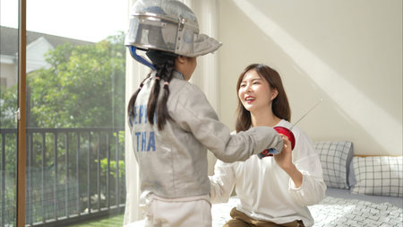 A girl in fencing gear with their mother preparing sports equipment before practicing fencing in...
