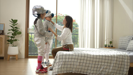 A girl and boy in fencing gear with their mother preparing sports equipment before practicing...
